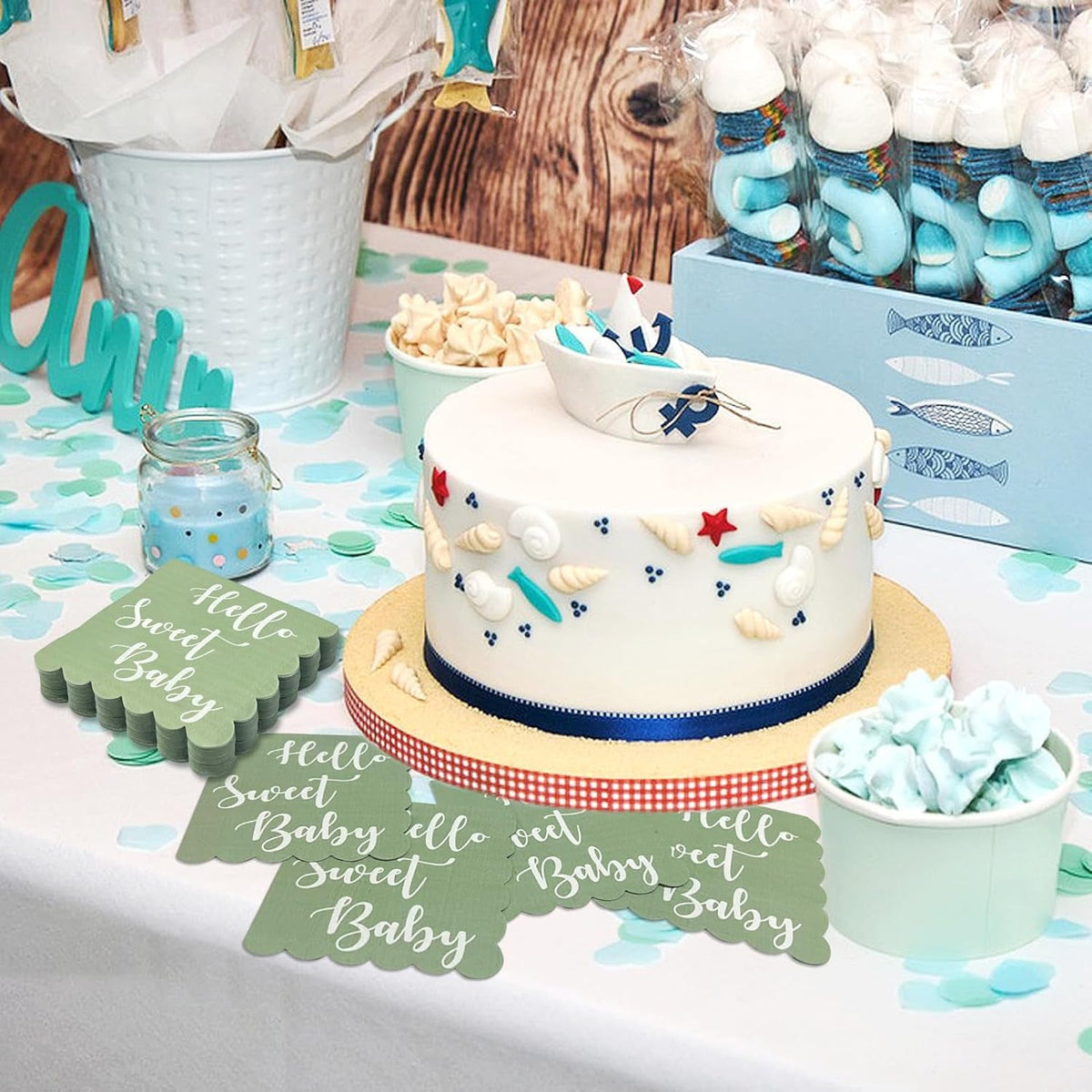 Mint green scalloped napkins on a table with a white cake decorated with a boat and blue accents, and other party treats.