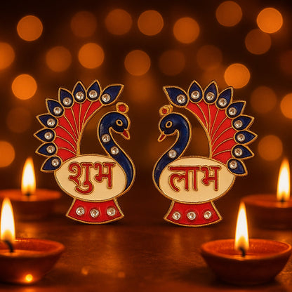 The two peacock Shubh Labh decorations are displayed with lit oil lamps and blurred background lights.