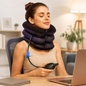 A woman with her eyes closed wears an inflatable neck traction device while sitting at a desk with a laptop.