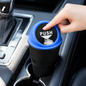 A hand pushes down on the blue lid of a black car dustbin, discarding a tissue inside a car's cup holder.