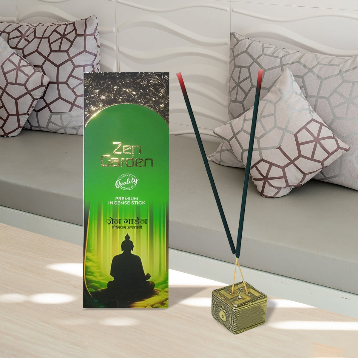 Two smoking green incense sticks in a gold holder next to a green box on a light wooden surface.