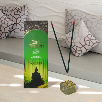 Two smoking green incense sticks in a gold holder next to a green box on a light wooden surface.