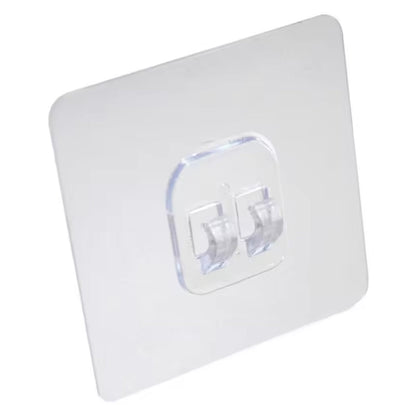A clear square self-adhesive wall hook with two transparent prongs is shown against a plain white background.