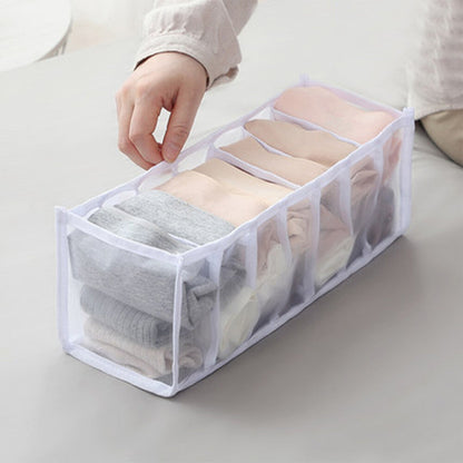 A person's hand adjusts a folded gray garment within a white mesh organizer, holding several items on a light surface.