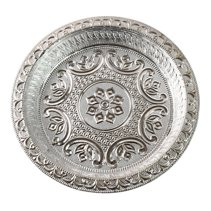 A top-down view of a round silver-colored plastic pooja thali with detailed embossed floral and geometric patterns on a