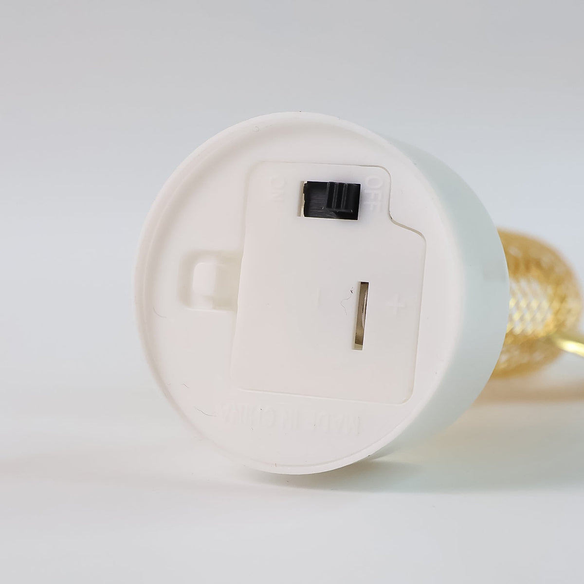 The underside of a white light base shows a battery compartment with an open lid and a black on/off switch.