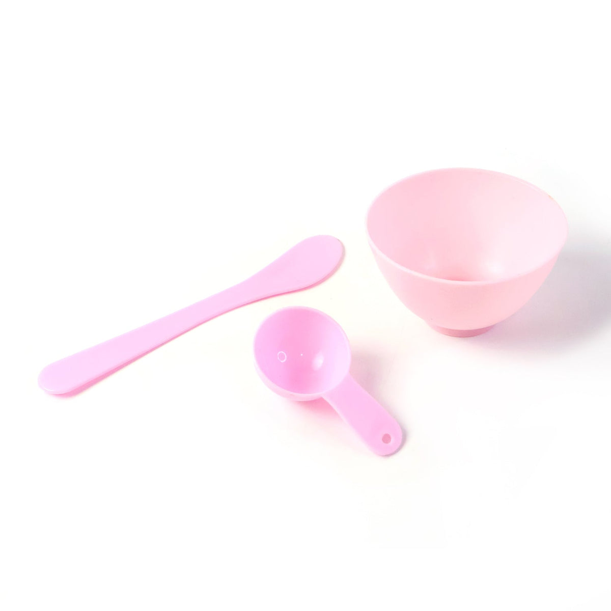 A pink mixing bowl, spatula, and measuring spoon are neatly arranged on a plain white background.