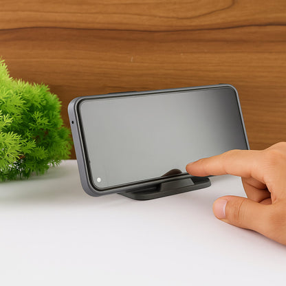 A hand touches the screen of a smartphone resting horizontally on a black mobile stand, next to a green plant.