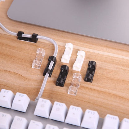 A mix of black, white, and clear plastic cable clips on a wooden desk next to a white keyboard and laptop.