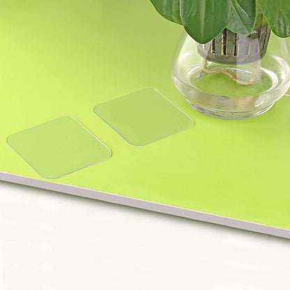Two clear adhesive squares are shown on a bright green surface next to a glass vase with a plant.
