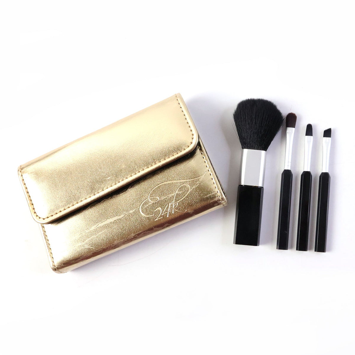 A gold makeup brush pouch with '24K' embossed and four black and silver brushes on a plain white background.
