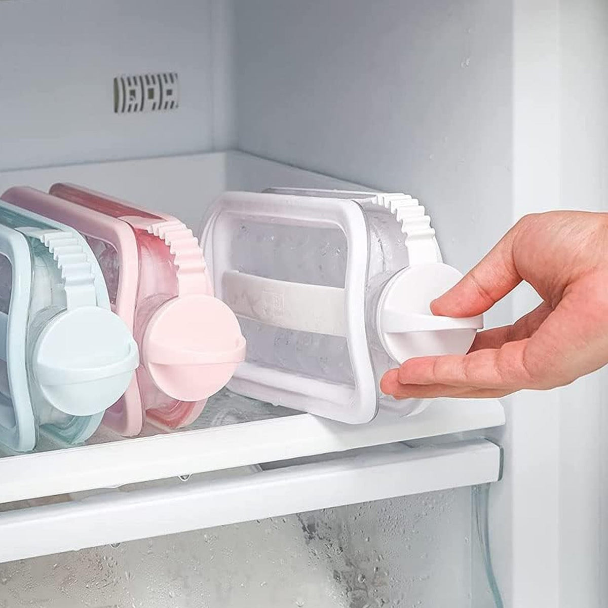 A hand places a white ice ball maker bottle into a refrigerator shelf, with other colored bottles visible in the background.
