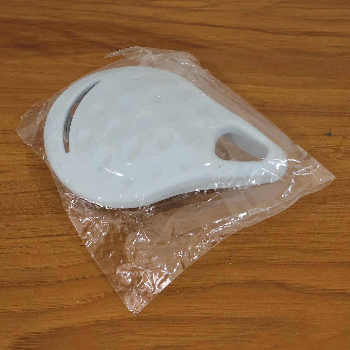 A light blue silicone scalp massager sealed inside a clear plastic package on a wooden surface.