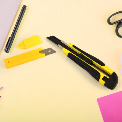 A yellow and black utility knife with a separate blade and yellow cover on a light yellow surface.