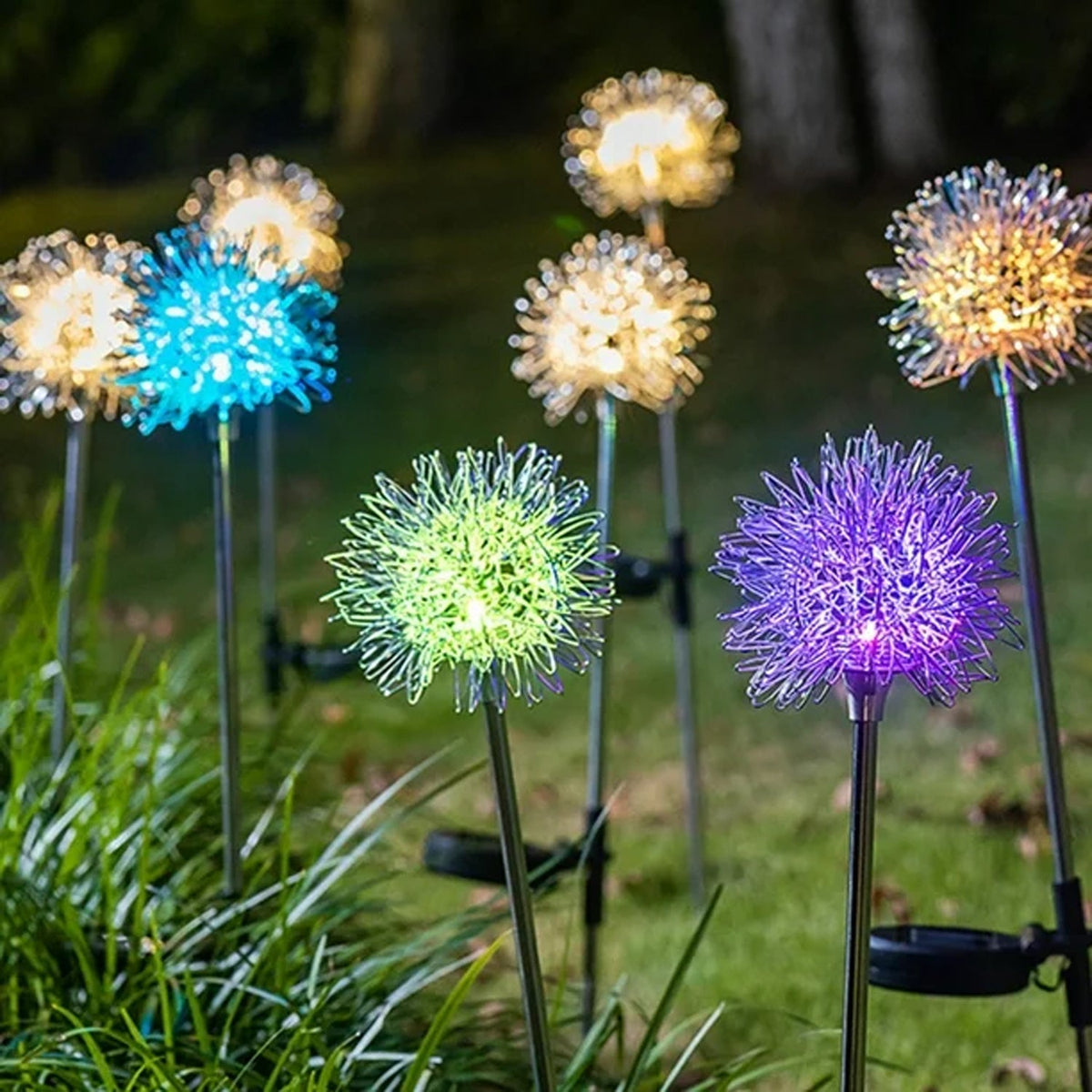 Multiple dandelion-shaped solar garden lights glow in various colors including blue, green, purple, and warm white in a