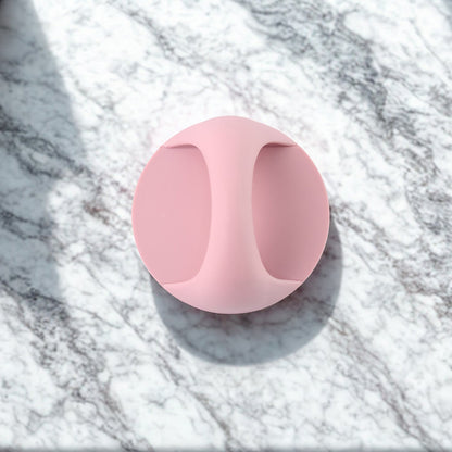 A pink self-adhesive handle lies flat on a white and grey marble surface with dappled shadows.