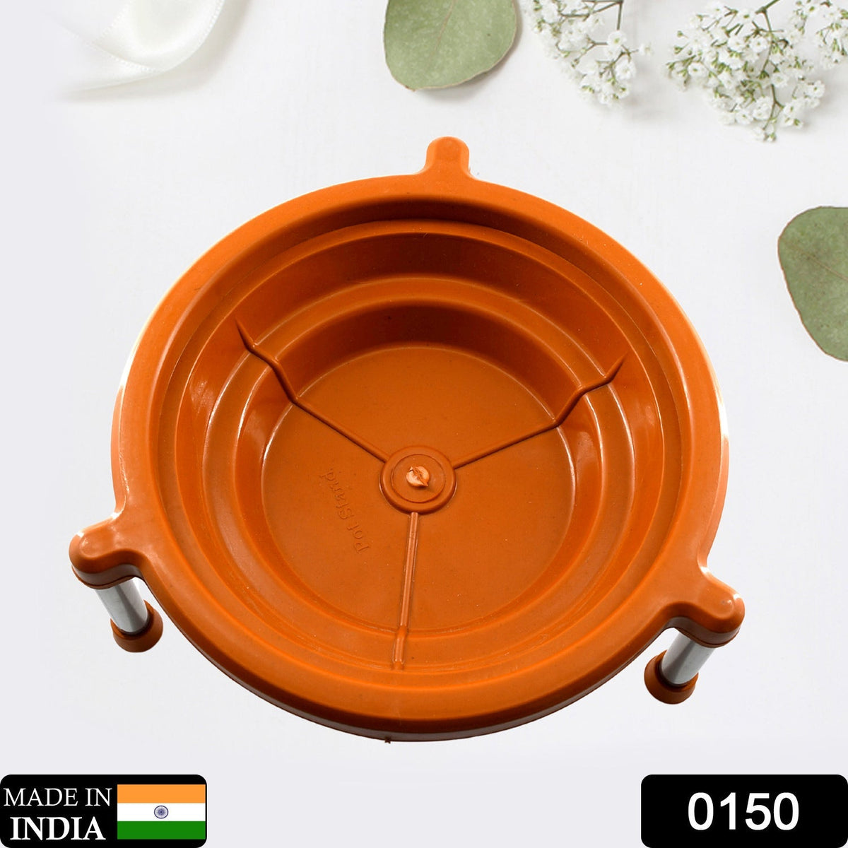 Overhead view of an orange plastic stand with three silver legs, on a white surface with green leaves.