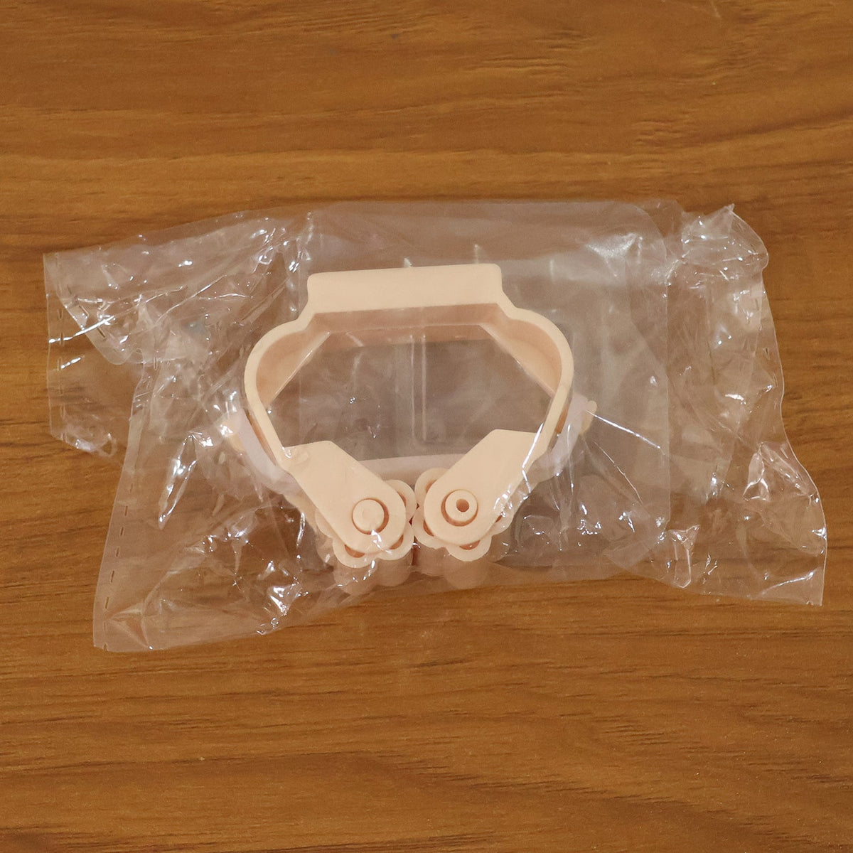 A single peach-colored broom holder is sealed inside clear plastic packaging on a wooden surface.