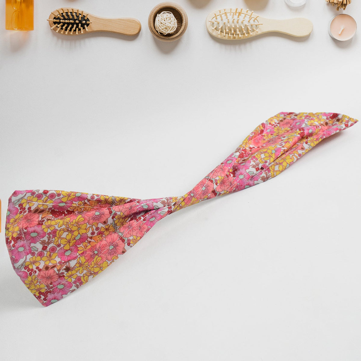 Pink and yellow floral hair bun maker laid flat on a white surface with various hairbrushes.