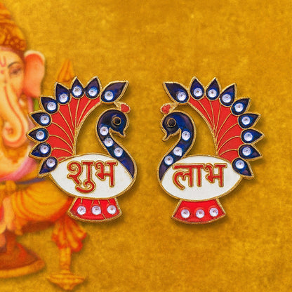 The two peacock Shubh Labh decorations are on a gold background with a blurred image of Ganesha to the left.