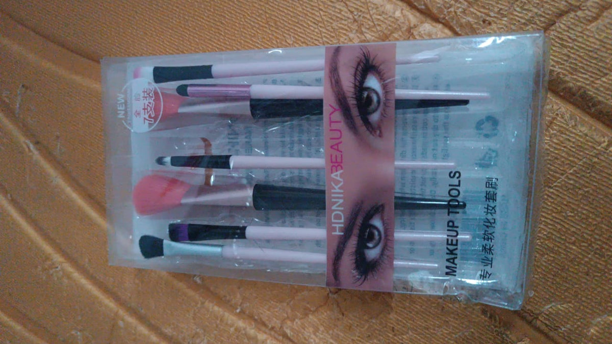 A clear plastic package containing seven makeup brushes is displayed on a textured brown surface.