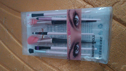 A clear plastic package containing seven makeup brushes is displayed on a textured brown surface.
