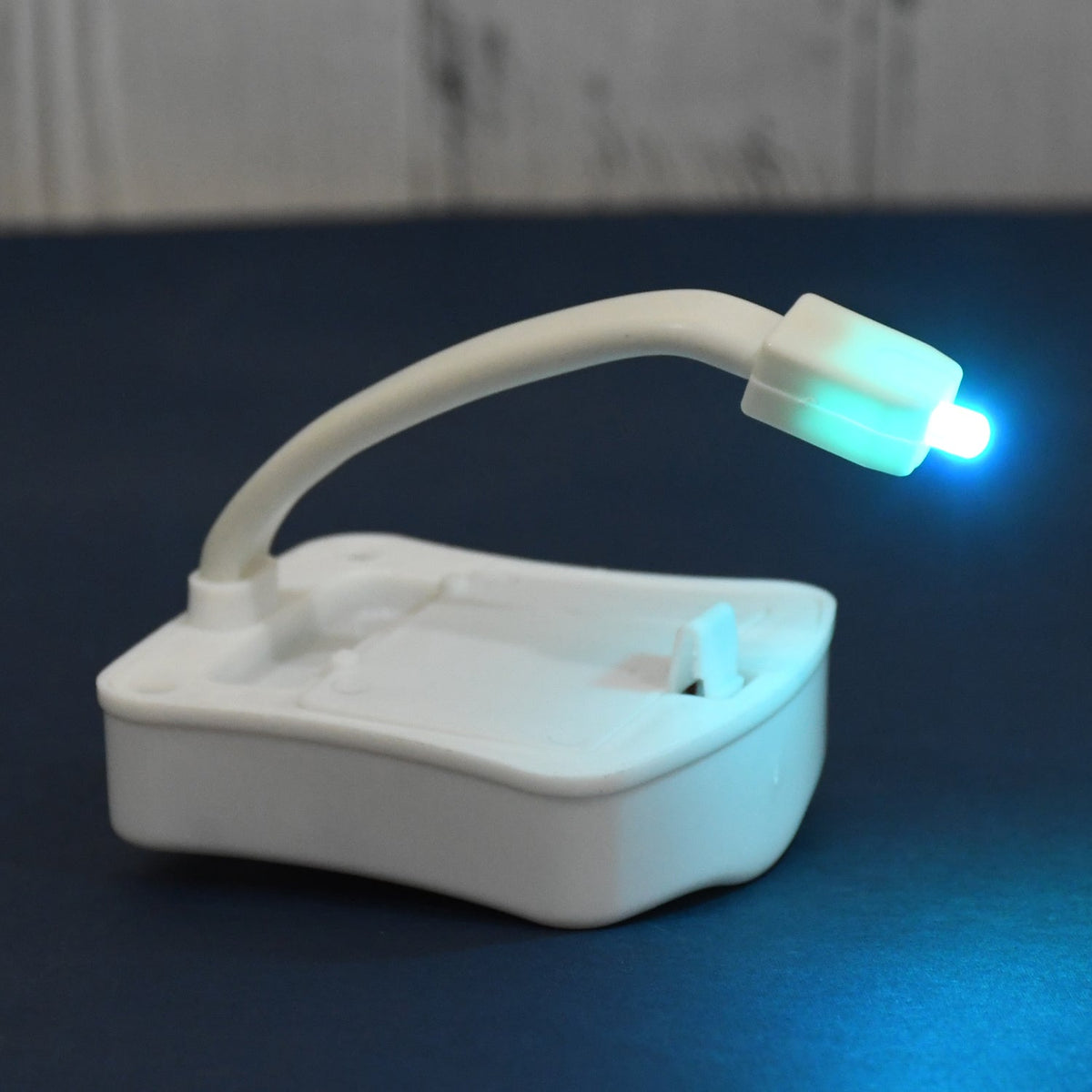 White motion sensor toilet light with a flexible arm, emitting a blue-green glow, on a dark blue surface.