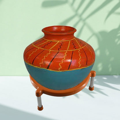 Decorated terracotta pot with red, blue, and yellow patterns on an orange plastic stand with silver legs.