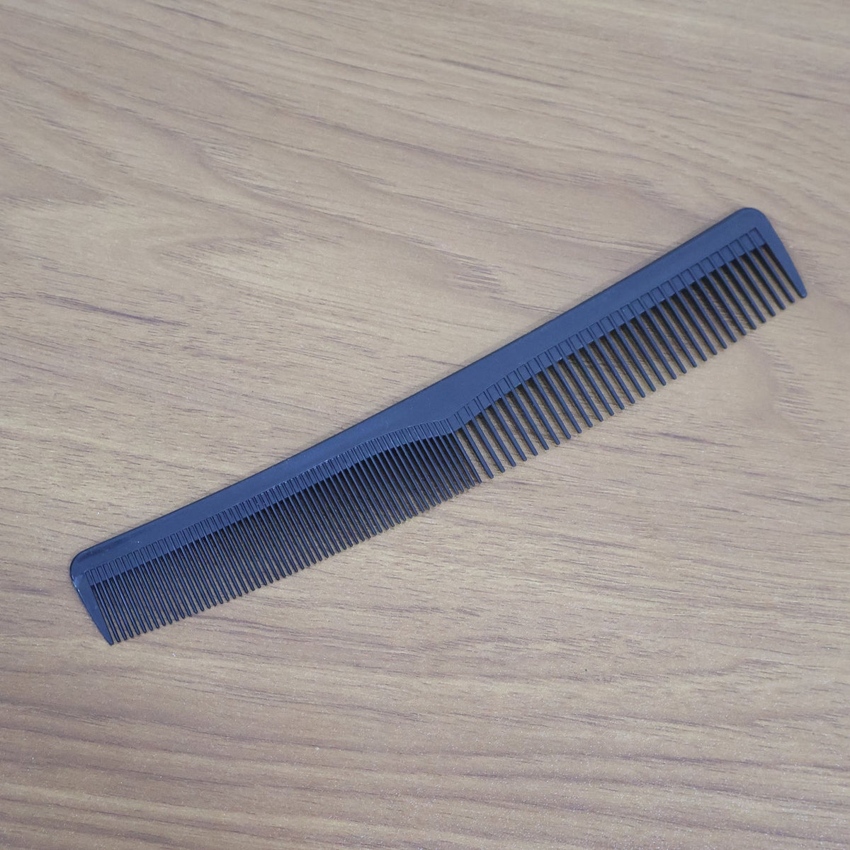 A blue dual-tooth comb is placed diagonally on a dark wooden surface.