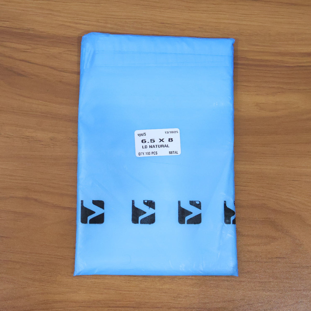 A light blue polybag with a white label showing size and quantity, and black logos at the bottom, on a wooden surface.