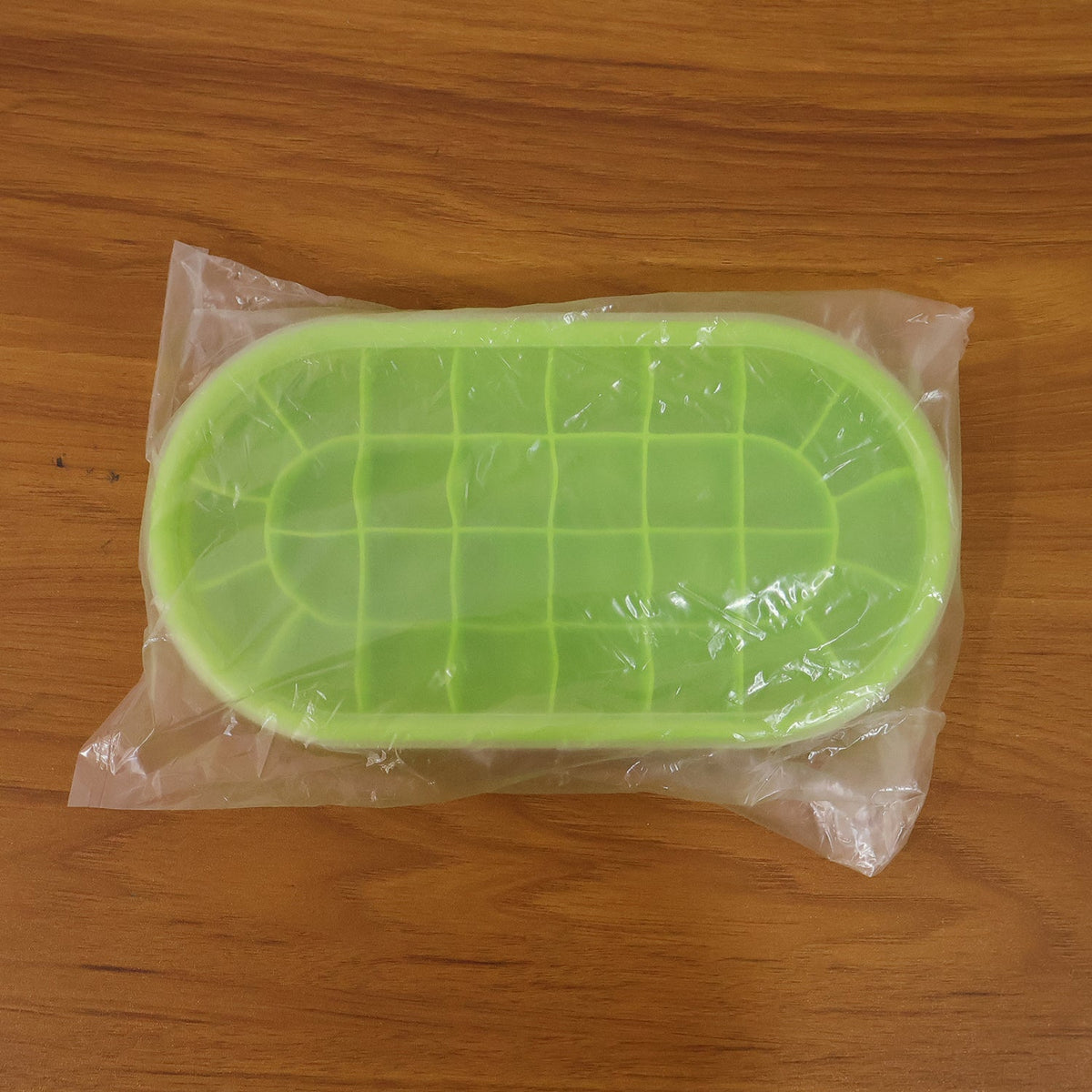 A green oval silicone ice cube tray sealed in clear plastic packaging, resting on a wooden surface.
