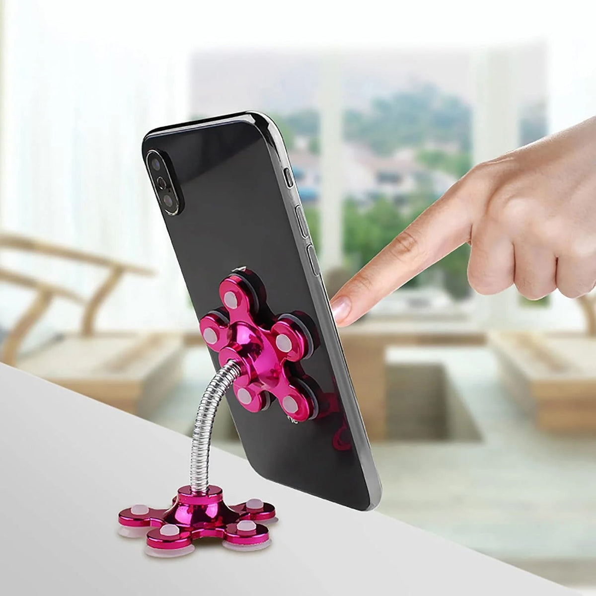 A hand points to a phone attached to a pink flower-shaped phone holder with a flexible silver arm.