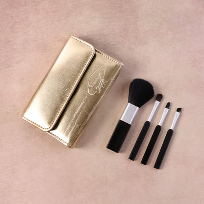 A gold makeup brush pouch with '24K' embossed and four black and silver brushes on a light pink surface.