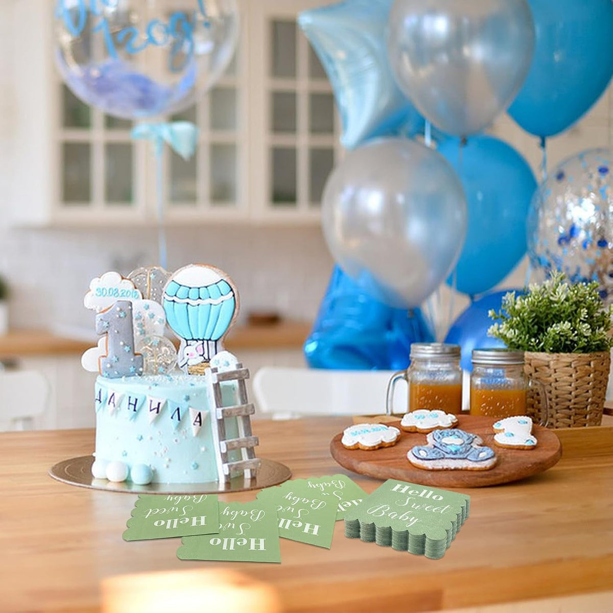 Mint green scalloped napkins scattered on a table with a blue birthday cake and blue balloons in the background.