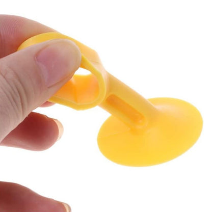 A hand holds a yellow silicone suction cup door stopper, showing its flexible material and design.