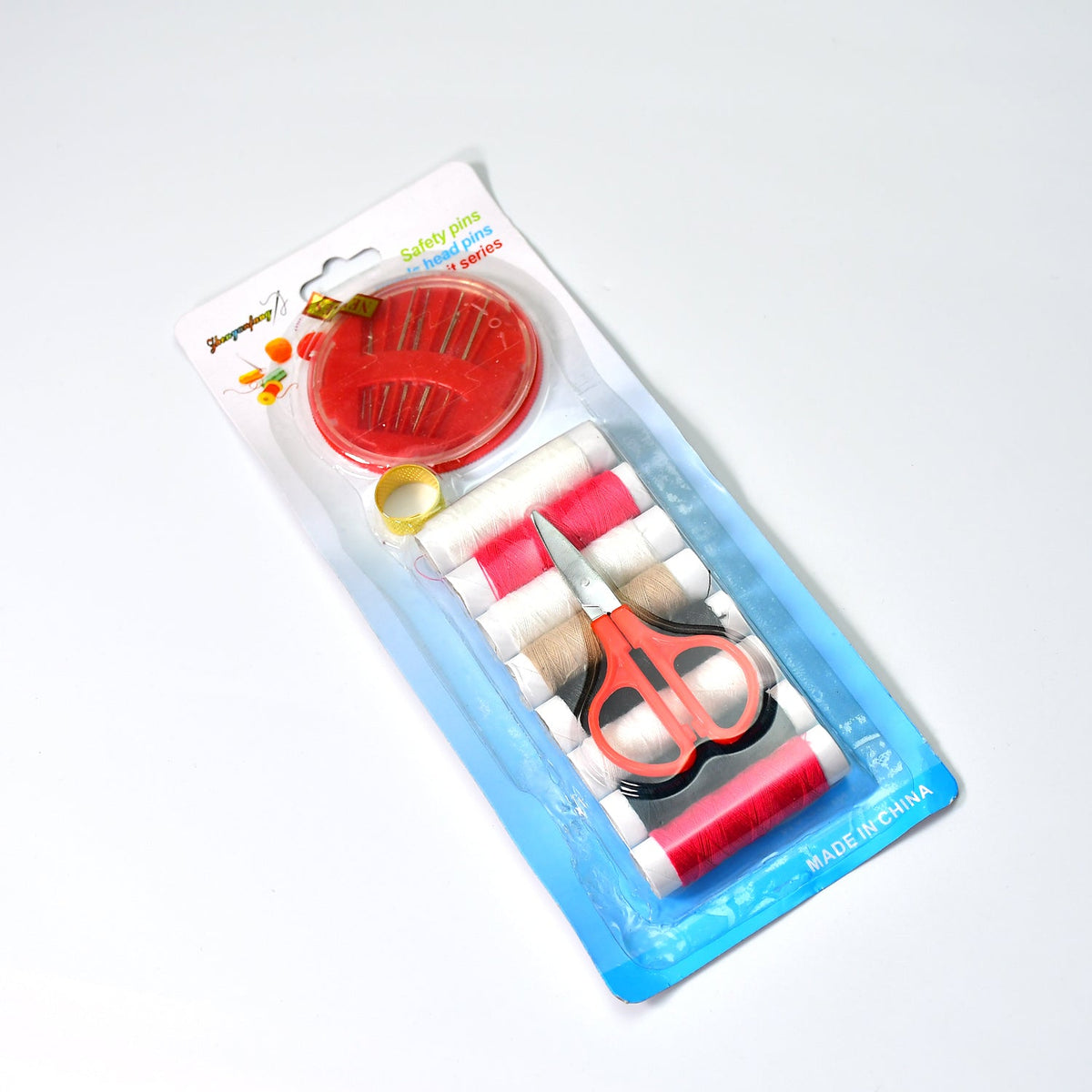 A clear plastic-packaged sewing kit containing thread, a thimble, scissors, and a needle holder.