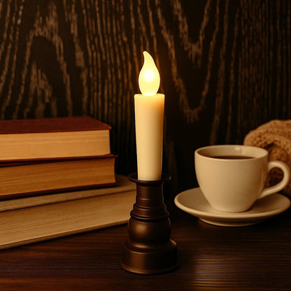 A cream LED candle with a flickering flame in a dark bronze holder, with books and a cup of coffee.
