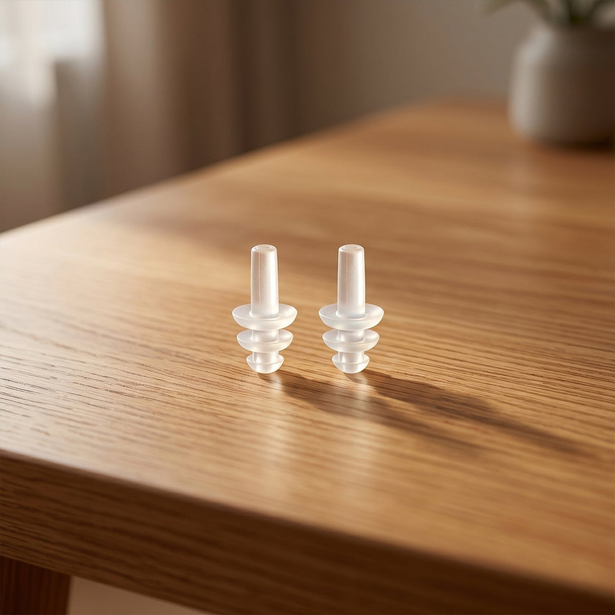 Two clear, ribbed silicone earplugs are placed upright on a light wooden table.