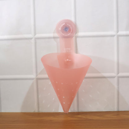 A pink silicone sink strainer with a suction cup, empty, attached to a white tiled wall above a wooden surface.