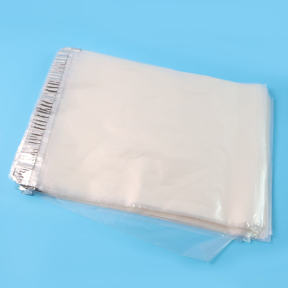 A stack of clear polybags with silver adhesive strips, angled on a bright blue background.