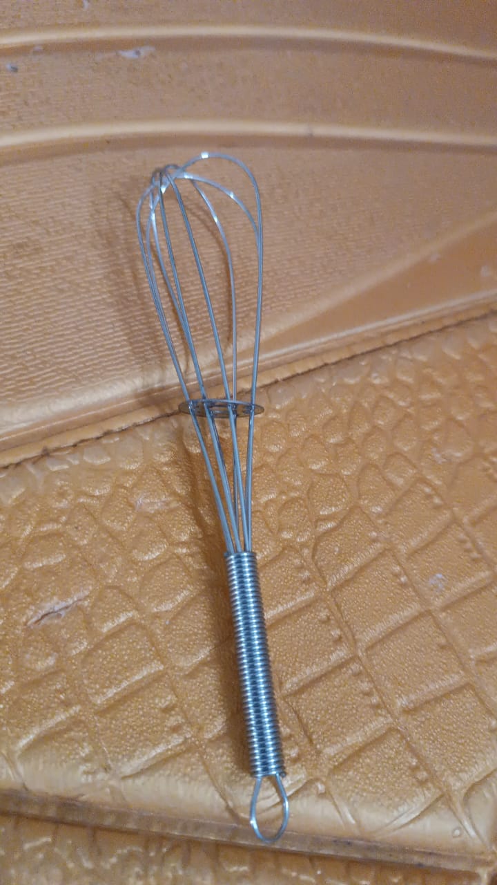 A small silver spring coil whisk rests on a textured golden-brown surface.