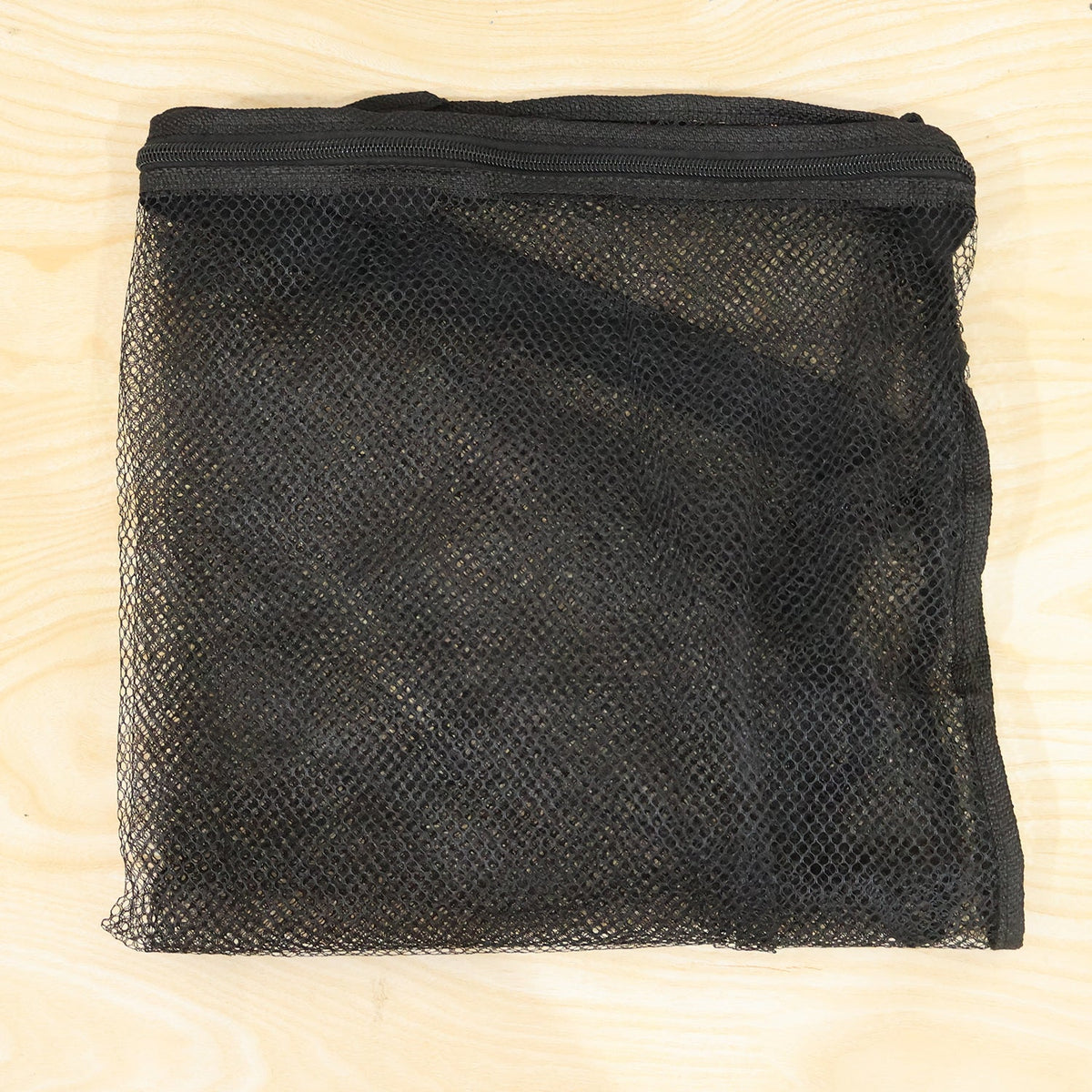 A folded black mesh zipper storage bag is laid flat on a light wood surface.