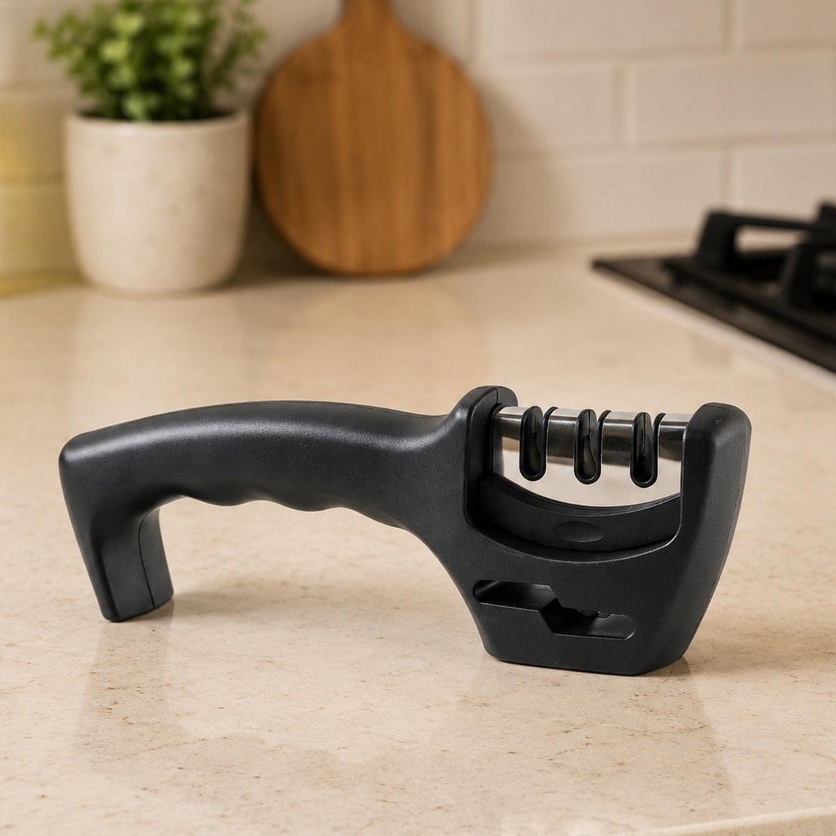 A black three-stage knife sharpener sits on a light speckled kitchen counter with a plant and cutting board in the
