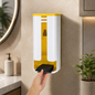 A hand pulls black plastic bags from a white and yellow wall-mounted dispenser in a bathroom setting.