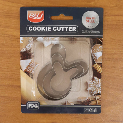 A packaged set of three stainless steel cookie cutters in an abstract, wavy shape on a wooden table.