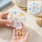 Hands dispensing yellow pills from a clear 7-day pill organizer with blue and yellow pills inside.