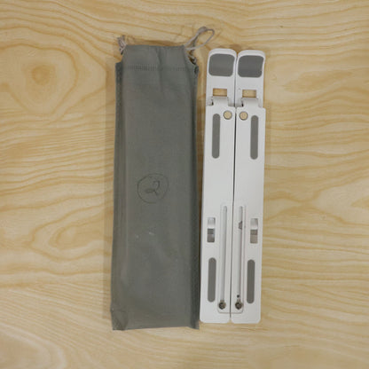 White folded laptop stand next to a gray fabric carrying pouch, both resting on a light wooden surface.