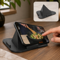 A black pyramid-shaped mobile stand holds a smartphone displaying a cooking video, with a hand touching the screen.