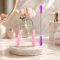 A pink and silver facial hair remover spring tool and a purple and silver facial hair remover stick on a marble stand.