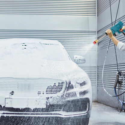 A person's hands hold a teal pressure washer, spraying water onto a white foamy car in front of a gray garage door.